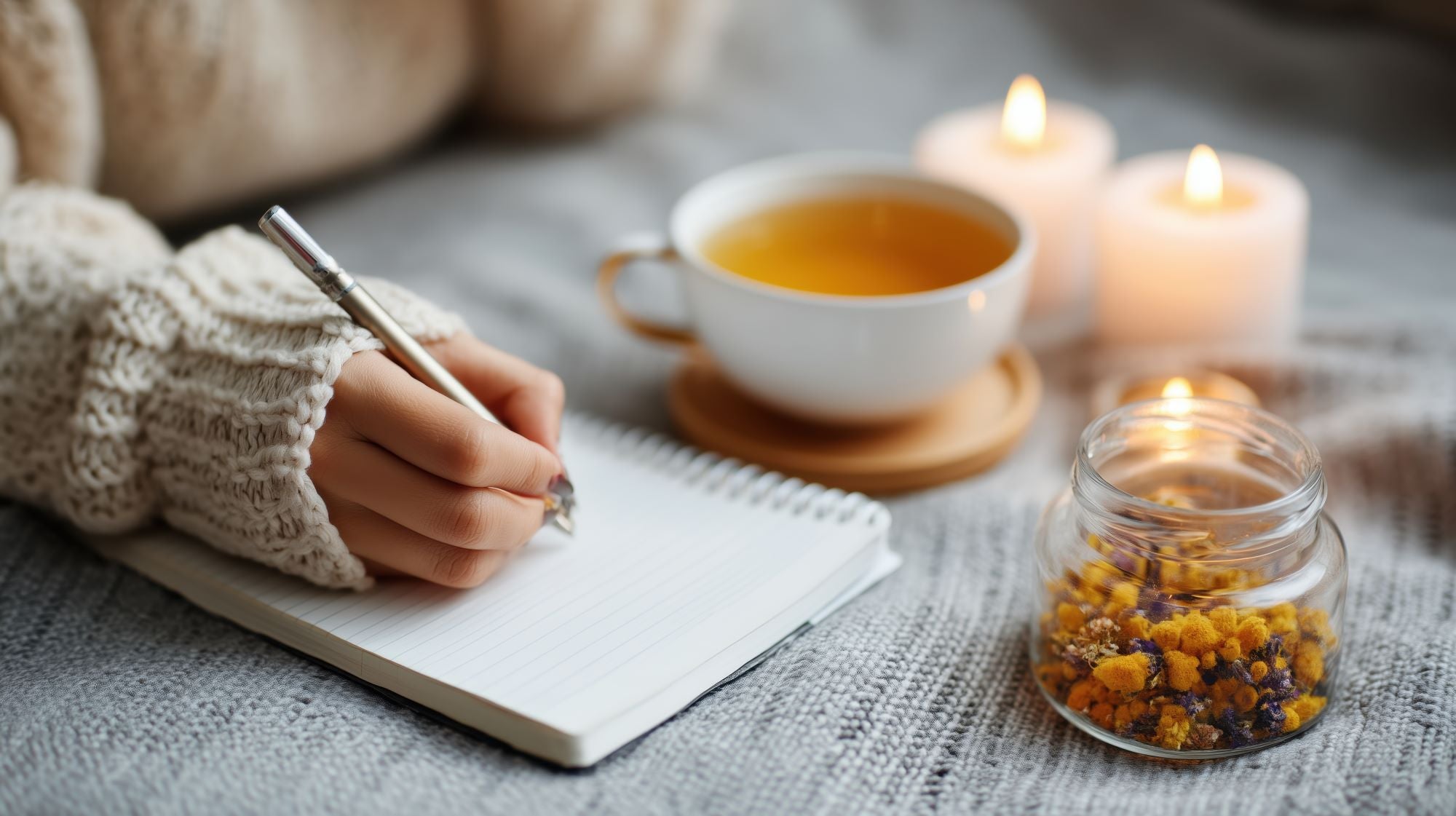 Person writing in a notebook with a cup of tea and candles in the background