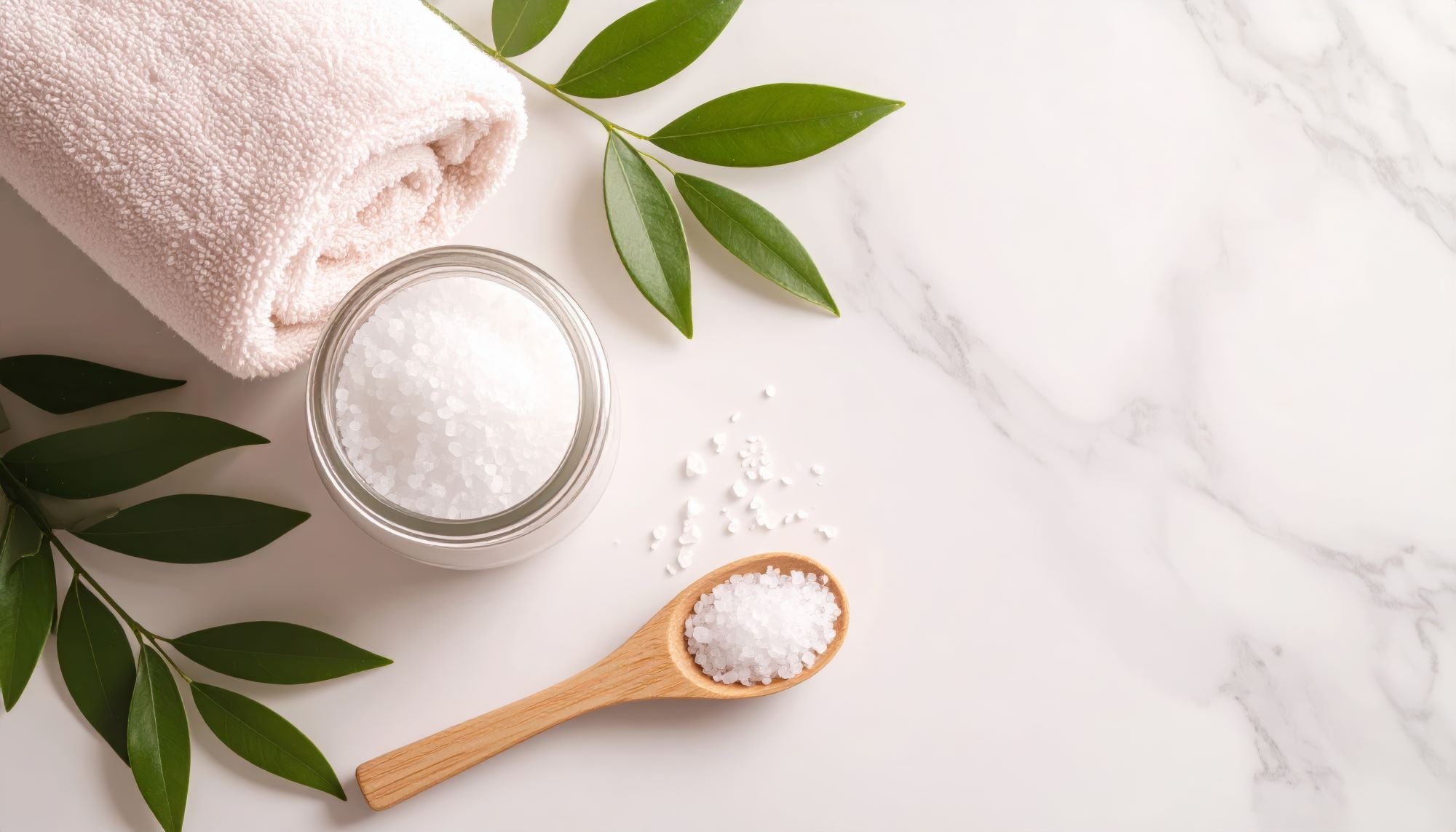 Jar of white powder with a wooden spoon, towel, and green leaves on a marble surface